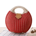 Red circular straw handbag with white handles on a rustic table in summer style - Red