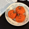 Three handmade orange wool felt pumpkin keychains with smiling faces on a ceramic plate - Pumpkin Trio