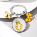 Detail of bee and honeycomb enamel keychain with glass dome and pearl bee charm - Letter O