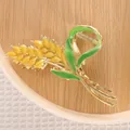 Close-up of a floral hair claw clip featuring golden wheat ears and green enamel leaves - Golden Wheat Ear