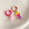 Detailed view of colorful asymmetric fish and star pendants on steel hoop earrings - Pink Fish Starfish Style