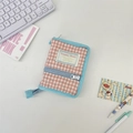 Close-up of pink checkered quilted binder cover with blue zipper and brand label on desk - Nude Pink