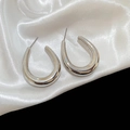 Macro detail of silver U-shaped earrings with a high-polished finish on white silk - Silver