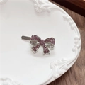 Detail of silver bow hair clip with purple rhinestones on a white ceramic plate - Bow / Purple