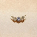 Elegante spilla ad ali d'angelo dorata con strass scintillanti su sfondo in tessuto beige - Oro