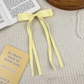 Detailed close-up of a pale yellow satin bow hair clip with long elegant ribbons - Yellow