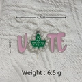 Detail view of pink and silver VOTE brooch with green leaf and small pearl accents - Silver/Pink AKA