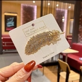 Élégante pince à cheveux plume dorée avec strass brillants sur carte de support - Plume Dorée
