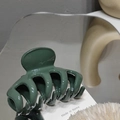 Detailed close-up of a glossy dark green shark hair claw clip on a stylish mirror surface - Bean Green