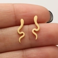 Minimalist gold snake stud earrings with polished S-curve design shown on finger - 674 Snake / Gold