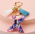Detail of letter X resin keychain with colorful shells, gold hardware and blue tassels - Letter X