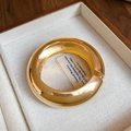 Dettaglio ravvicinato di un bracciale rigido dorato lucido in un portagioie in legno. - Stile 32 - Oro