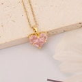 Gros plan d'un collier doré avec un pendentif en cristal rose taillé en cœur - Petit Cœur