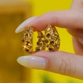 Golden hoop earrings with champagne zircon stones held by fingers on yellow background - Light Burgundy Champagne