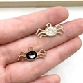Detail of gold alloy spider and black smiling face charms held in hand for DIY jewelry - Black Spider