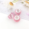 Three pink faceted resin charms with silver metal cores on light wood and daisy background - Pink
