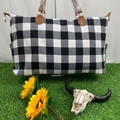 Detail of checkered weekender bag with brown leather handles on green grass background - Black & White Check