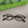 Flat lay of oval tortoiseshell glasses on desk with green packaging box details - Cream Marbled Clear Lens