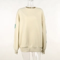 Close-up of cream crewneck sweatshirt showing fabric texture and green sleeve print detail - XS / Apricot
