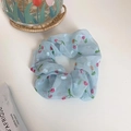 Light blue organza scrunchie with red cherry and white flower print on white desk - Ripe Cherry Blue