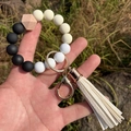 Close-up of silicone beaded keychain bracelet with wood bead and white tassel detail - Black and White