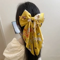 Large yellow satin bow hair clip with floral print on woman's hair back view - Yellow