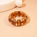 Dettaglio di segmenti in acrilico ambra e anelli in metallo oro su bracciale rigido - Marrone