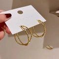 Detail of gold double-hoop earrings with hammered texture on a model hand - Gold Double Cross Hammered Pattern