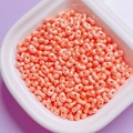 Close-up of pearlized coral pink peanut shaped dual-hole beads for DIY jewelry making - Light Orange
