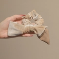 Elegant beige velvet bow scrunchie with a gold tag and subtle shimmering finish - Beige