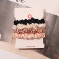 Detail view of 4-pack satin scrunchies in black, cream, gold, and pink on card - Black Cream Champagne Snow Ivory