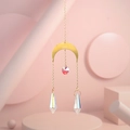 Detail of golden moon suncatcher with iridescent crystal prisms on pink geometric background - US 10