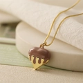 Macro detail of brown heart pendant with golden lava drip effect on a dainty gold chain - Camel