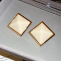 Gros plan sur les boucles d'oreilles pyramides en résine crème avec bordure dorée - Beige/Or