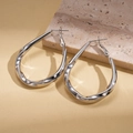 Detail shot of silver twisted teardrop hoop earrings on natural travertine marble background - Silver