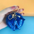 Close-up of blue fluffy pompom keychain with gold hardware and glittery resin letter W - Letter W