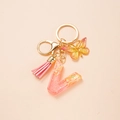 Pink resin letter V keychain with gold butterfly charm and tassel on pink background - Letter V