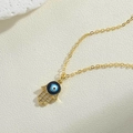 Makro-Detail des goldenen Hamsa-Handanhängers mit blauem Auge und funkelnden Zirkonen - Schwarze Hamsa-Hand