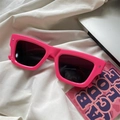 Macro view of thick pink frame sunglasses with dark lenses on a white fabric background - Rivet Square / Rose Red