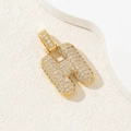 Gold-plated letter H pendant necklace with sparkling cubic zirconia on a beige background - Letter H