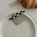 Detail view of a checkered acetate hair comb with sturdy metal teeth on a ceramic plate - Checkered