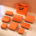 Detail van luxe oranje en zwarte sieraden ladekasten met bijpassende papieren geschenktassen - Deksel- en bodemdoos met logo / 5*5*3cm