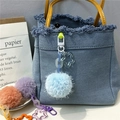 Detail of colorful plush pom-poms and stars on a denim bag with French decor background - Sky Blue