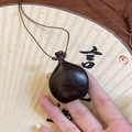 Gros plan d'un pendentif en bois sculpté tenu à la main avec un cordon ajustable - Noir