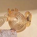 Vista dettagliata del bracciale rigido dorato a spirale con ombra artistica su sfondo di pietra - Oro