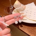 Elegant silver bow earrings with lustrous white pearls held by hand for display - Silver Bowknot Pearl Pair