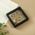 Schwarzer PE-Folien-Schmuckrahmen mit Strasssteinen und Ringen auf beigem Lederhintergrund - Schwarz (Schwebende Box) / 7*7*2cm