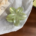 Green flower-shaped hair claw clip with pearlescent finish on a white paper background - Green