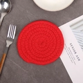 Handwoven round red cotton rope coaster with spiral pattern on dark textured table - True Red