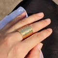 Gedetailleerde close-up van een brede gouden lava ring met gehamerd oppervlak aan de vinger - Goud
